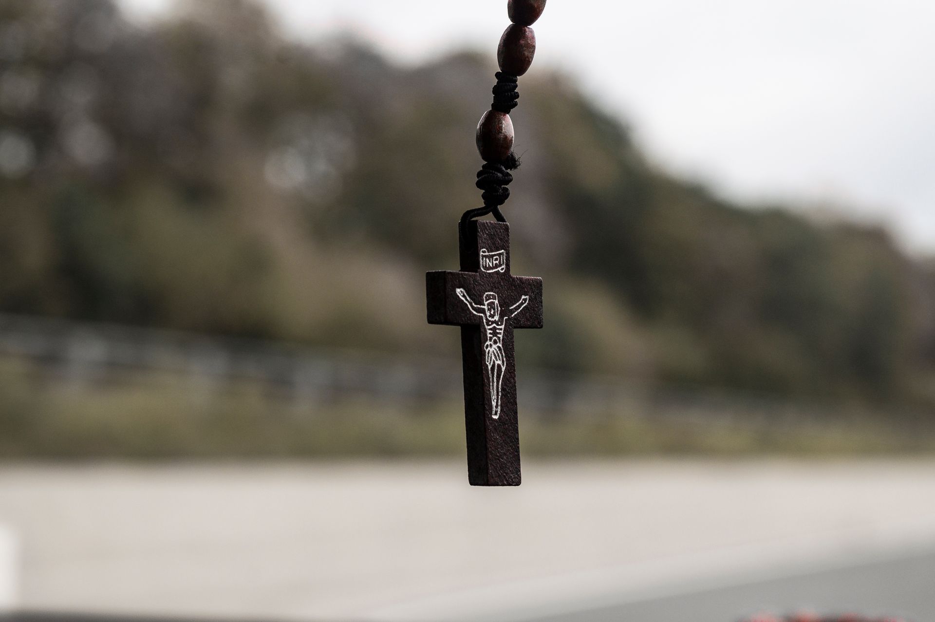 Detailed close-up of a wooden crucifix hanging with a blurred outdoor background.