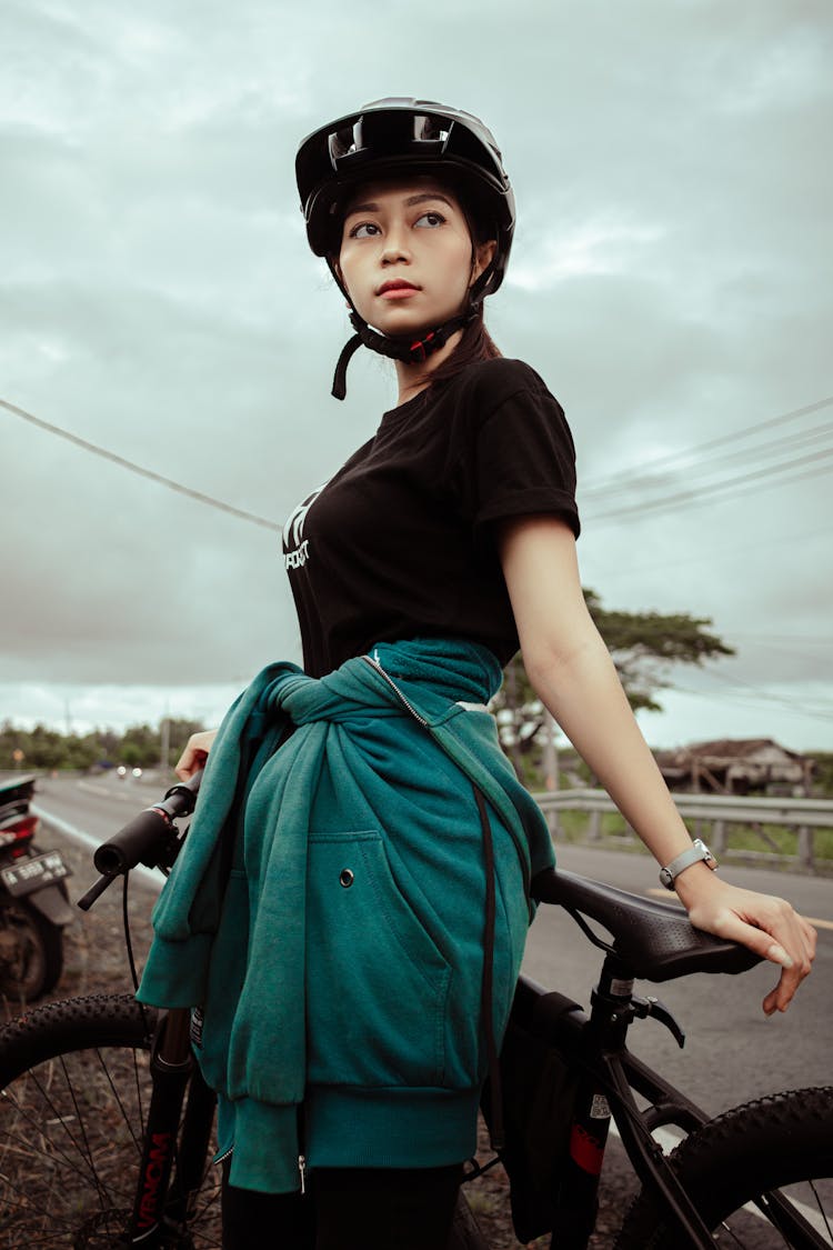 Low Angle View Of Woman In Helmet Leaning Against Bicycle By A Road