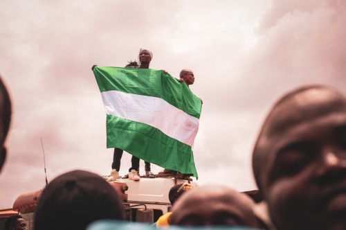 Free Two men standing on a vehicle, proudly holding the Nigerian flag against a cloudy sky. Stock Photo