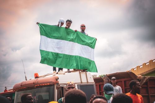 Free A group of people holding a Nigerian flag, standing on a vehicle in an urban setting, expressing national pride. Stock Photo