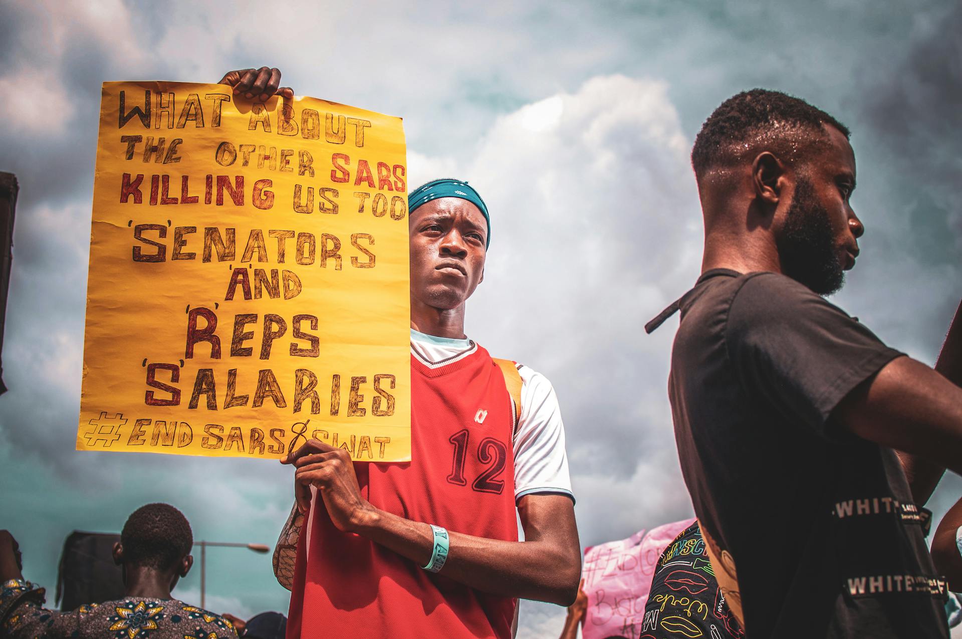 A man holding a protest sign against SARS in a public demonstration under cloudy skies.