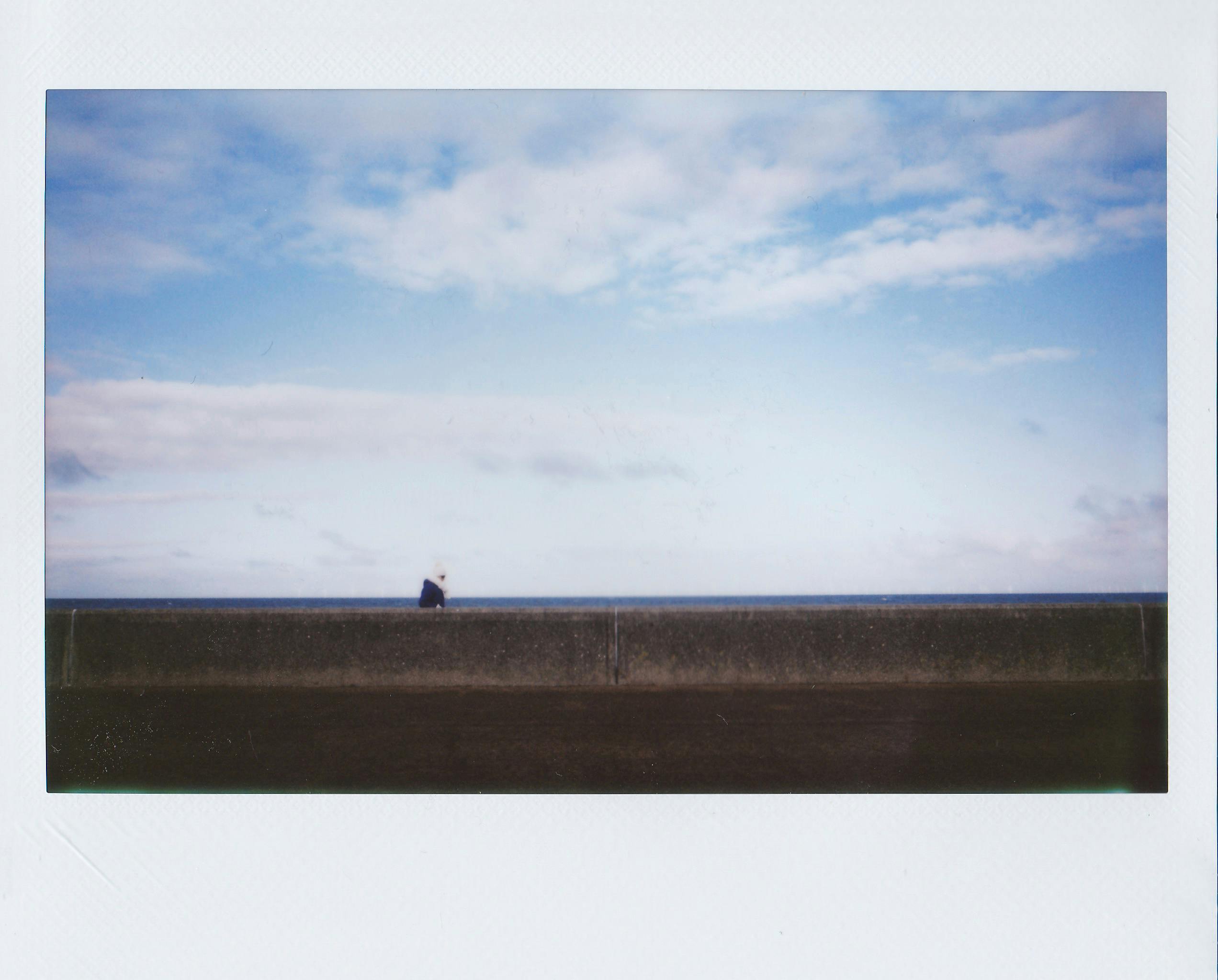 A lone figure walking along a coastal wall under a serene blue sky.