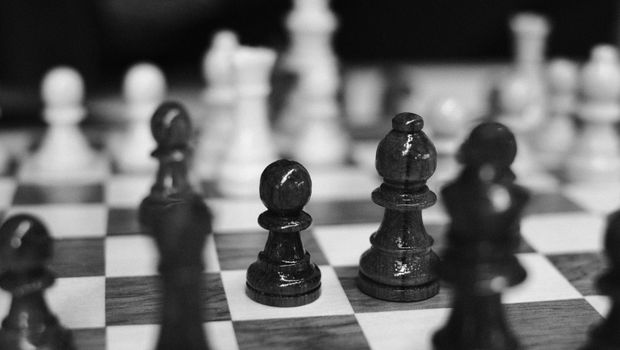 Black and white of wooden chessboard with placed chess pieces against blurred background