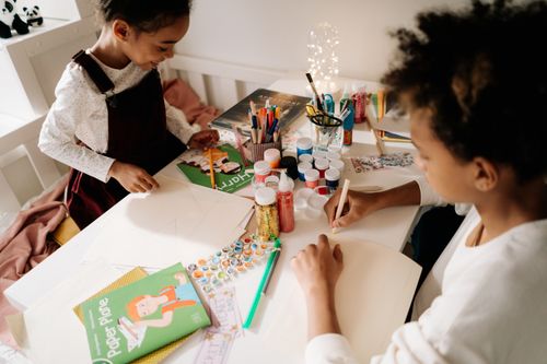 Free Two children enjoying arts and crafts with vibrant materials on a table indoors. Stock Photo