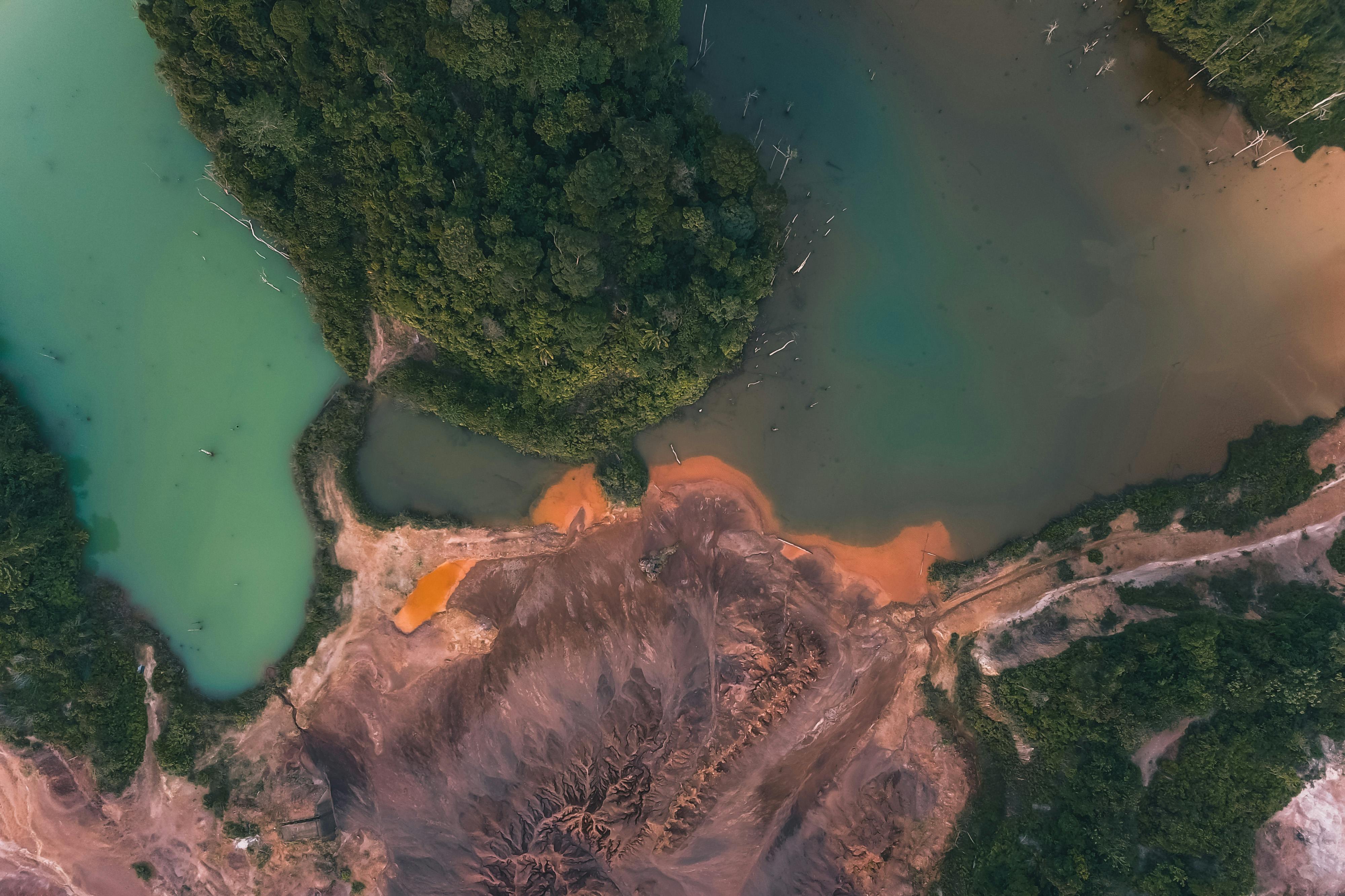 Aerial view of turquoise water washing green woodland and rough tropical terrain with dry sand