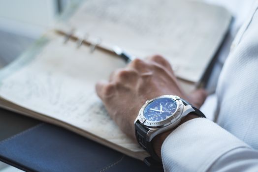 Detailed shot of a wristwatch and an open leather-bound notebook, showing a handwritten page.