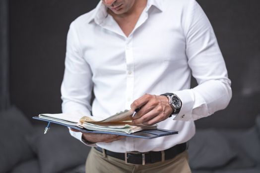Businessman in a white shirt reviewing documents from a planner or binder.