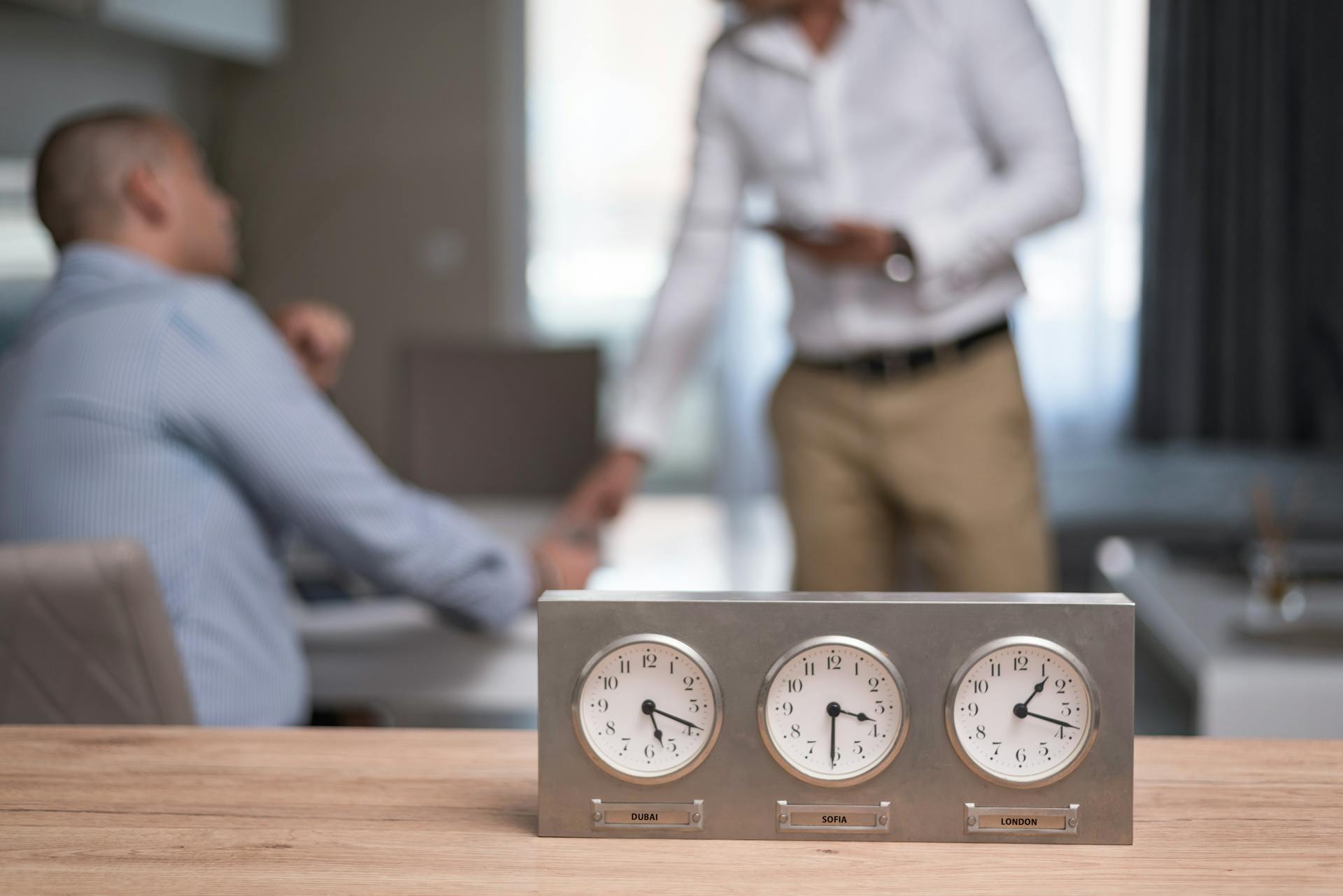 Two businessmen in an office with clocks showing different time zones, symbolizing global business.