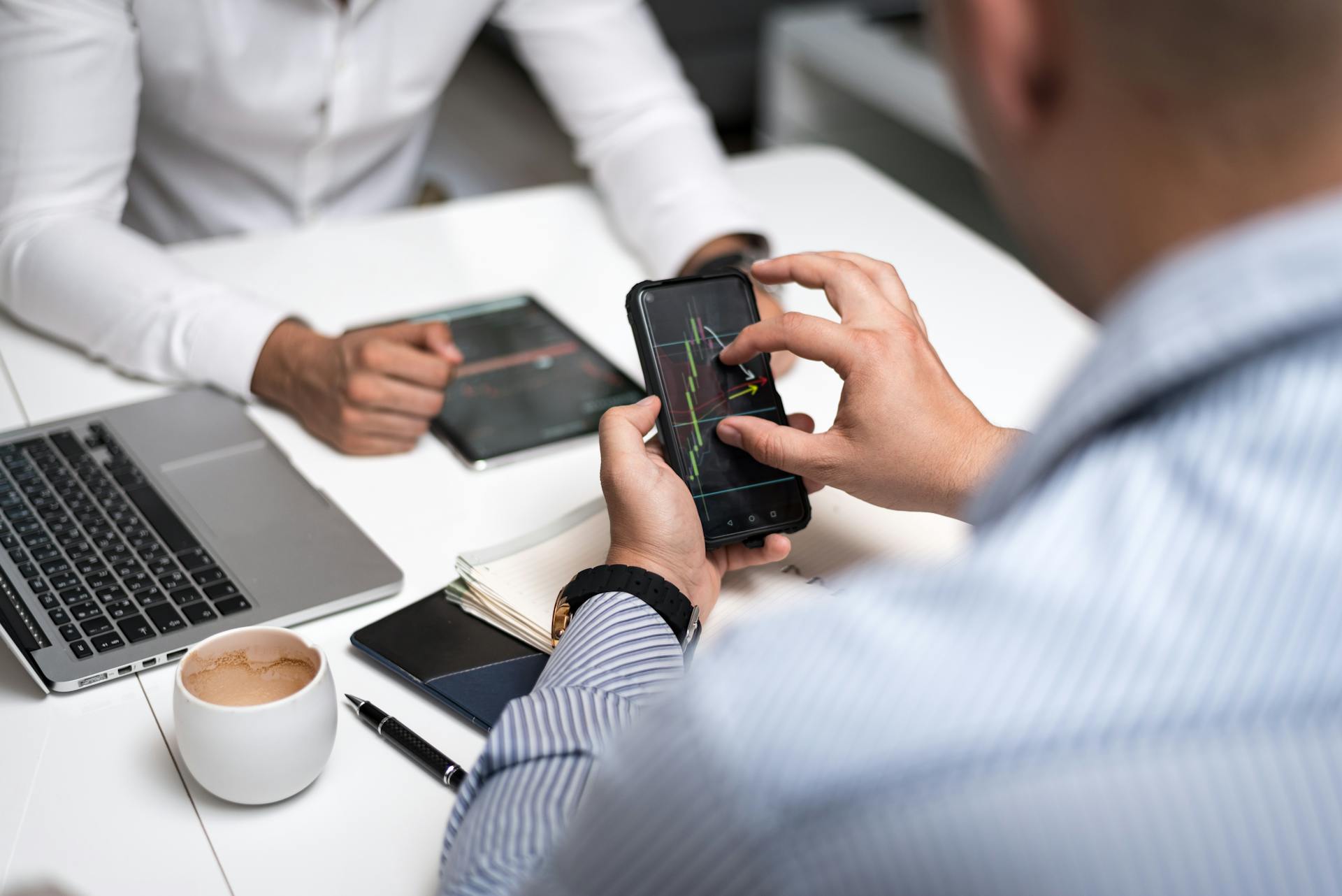 Business professionals using smartphones and tablets to analyze trading charts during a meeting.