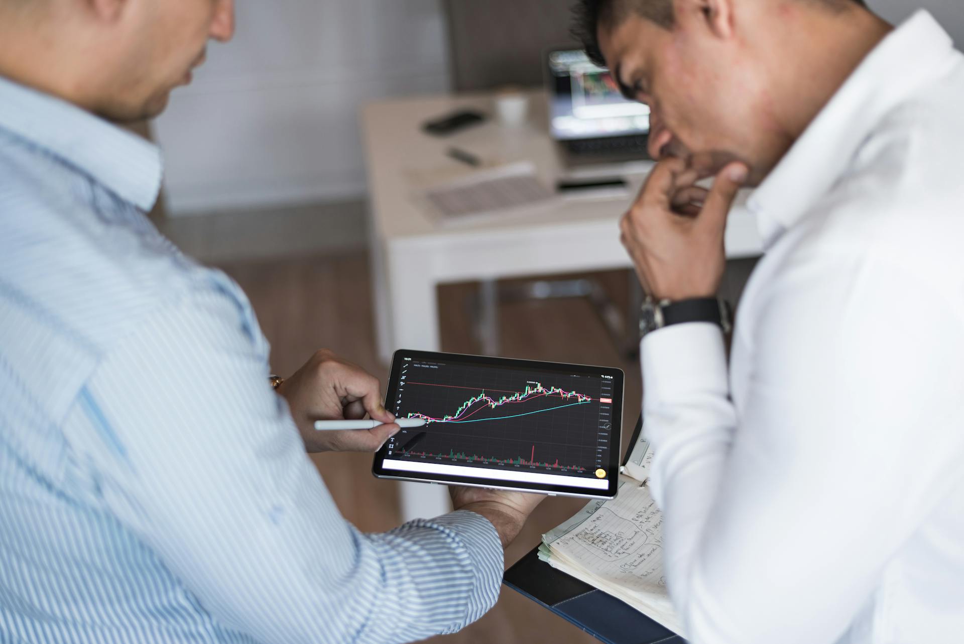 Two businessmen using a tablet for online trading analysis in an office setting.