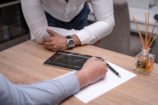 Two business professionals discuss data on a digital tablet at a wooden desk.