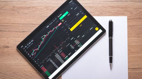 Overhead view of a digital tablet displaying stock market graphs and data on a wooden desk.