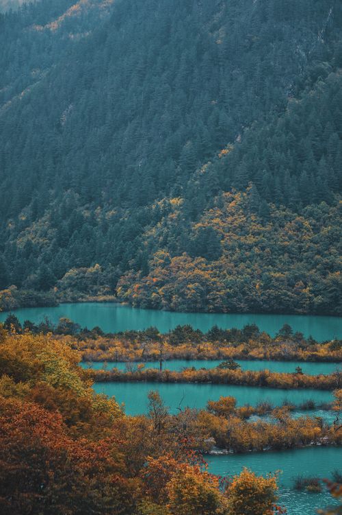 Free A serene autumn landscape with a turquoise lake surrounded by vibrant foliage and mountain hillsides, ideal for nature lovers. Stock Photo