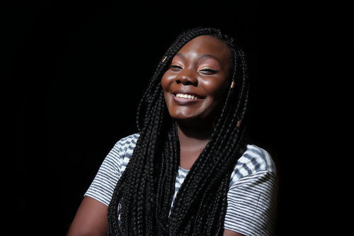 Free A joyful woman with braided hair smiling confidently against a black background. Stock Photo