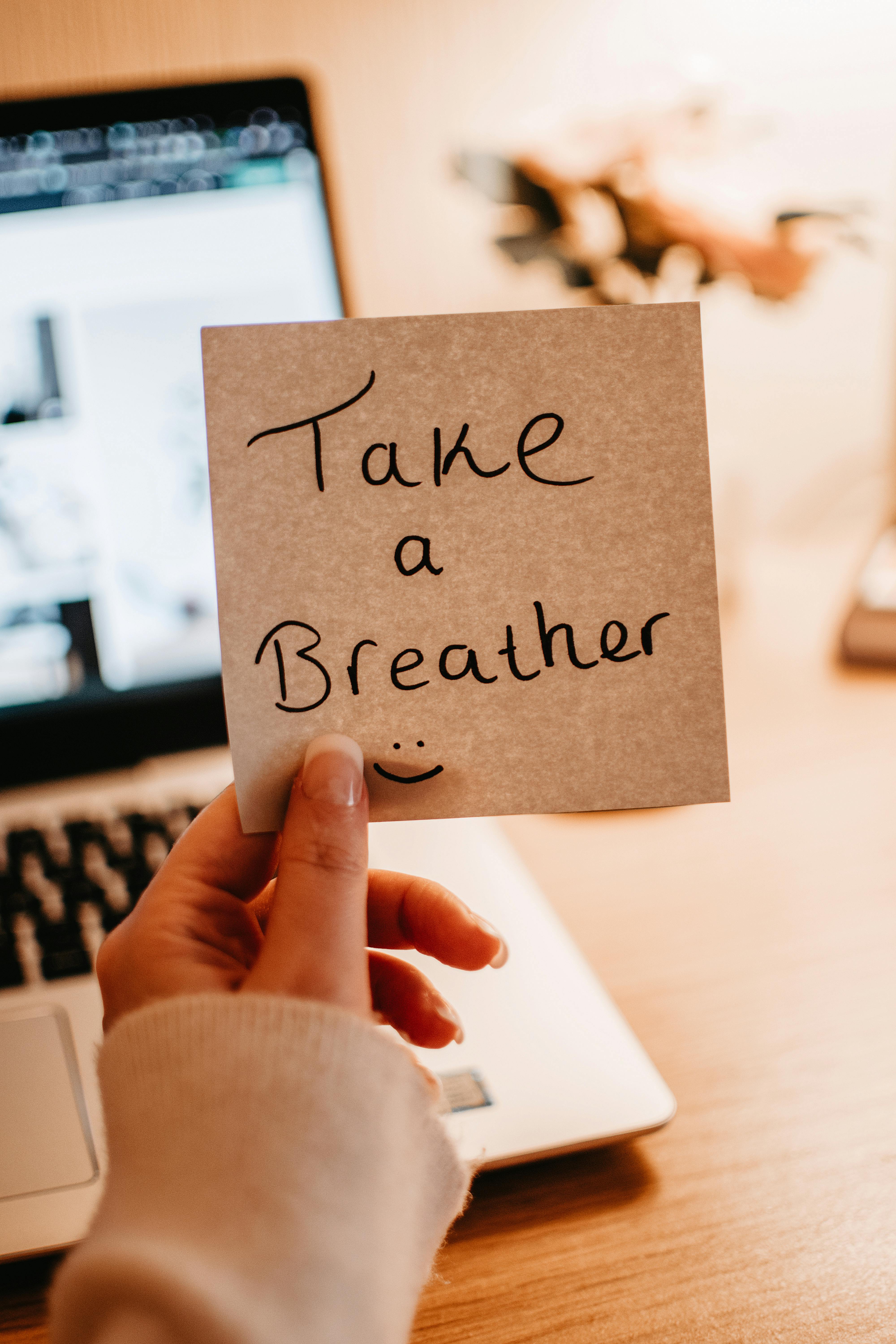 Hand holding a motivational note in a cozy home office setting.
