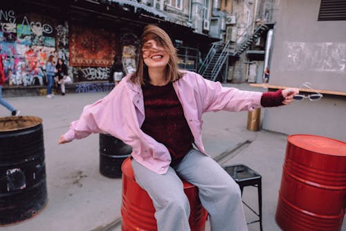 Happy young female with toothy smile and messy hair sitting on metal barrel