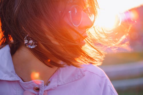 Crop calm female in modern sunglasses and messy flying hair lightened by sunlight at sundown