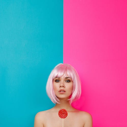 Woman with pink hair and makeup against bright wall