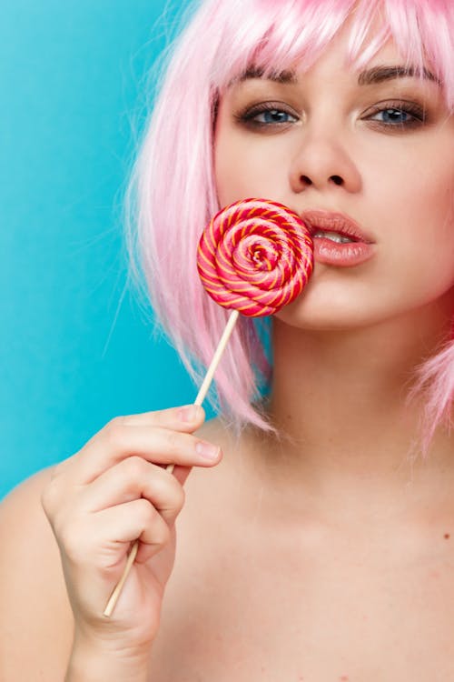 Crop young female with makeup and bare breast holding lollipop on stick against blue background