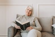 Senior woman with white hair enjoys a book while sitting on a comfortable sofa indoors.