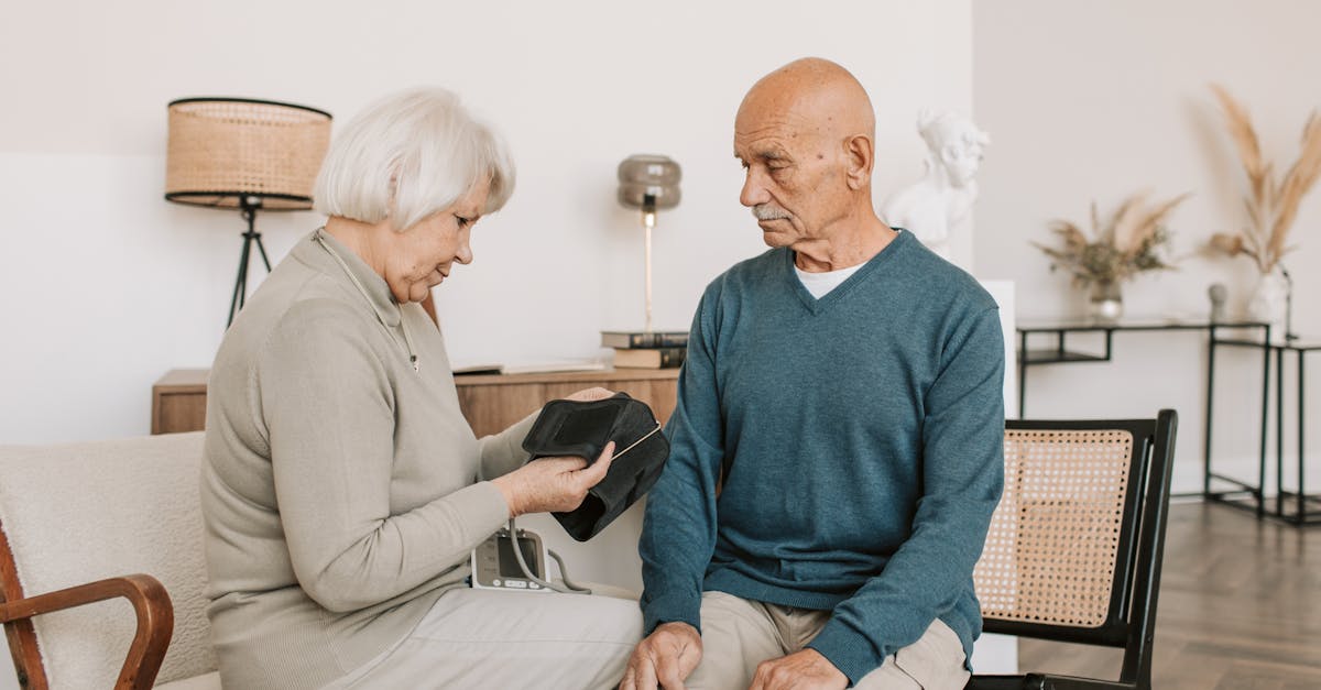 Elderly couple seated together, checking blood pressure with a sphygmomanometer indoors.