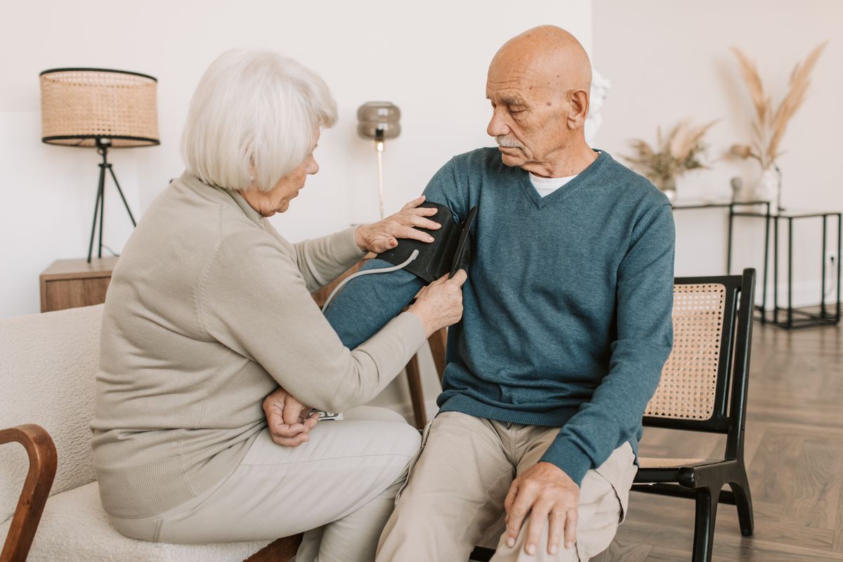 An elderly woman helps an elderly man check a wearable health device at home