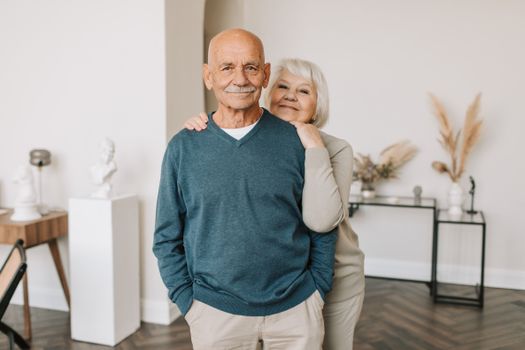 A smiling elderly couple embracing happily indoors, showcasing love and togetherness.