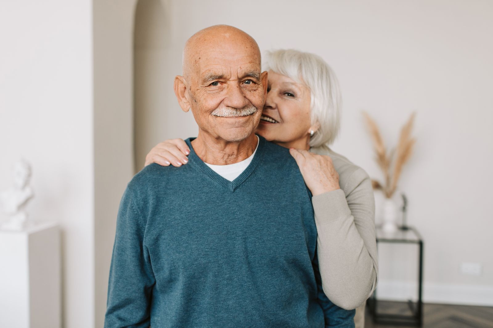Man in a blue v-neck sweater and a woman in a brown long-sleeve shirt smiling together