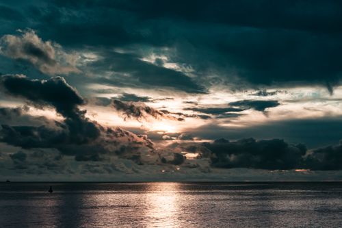 Free Majestic clouds casting a vivid display over a tranquil ocean at sunset. Stock Photo