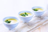 Three bowls of creamy parsnip soup garnished with fresh parsley on a rustic wooden surface.