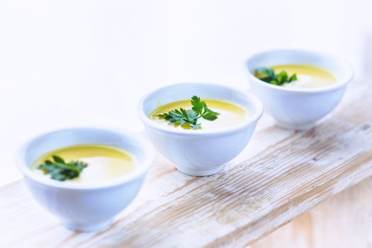 Three bowls of creamy parsnip soup garnished with fresh parsley on a rustic wooden surface.