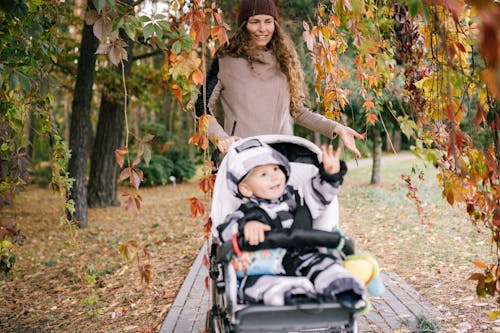 Happy Mother Walking in Fall Park with Child in Stroller