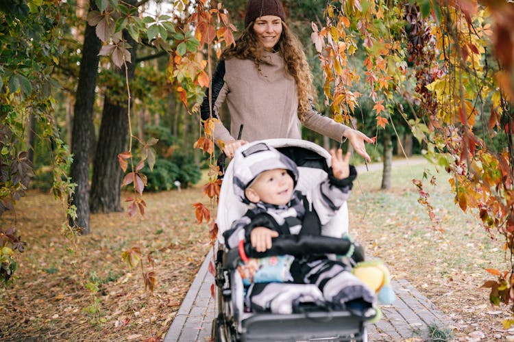 Happy Mother Walking In Fall Park With Child In Stroller