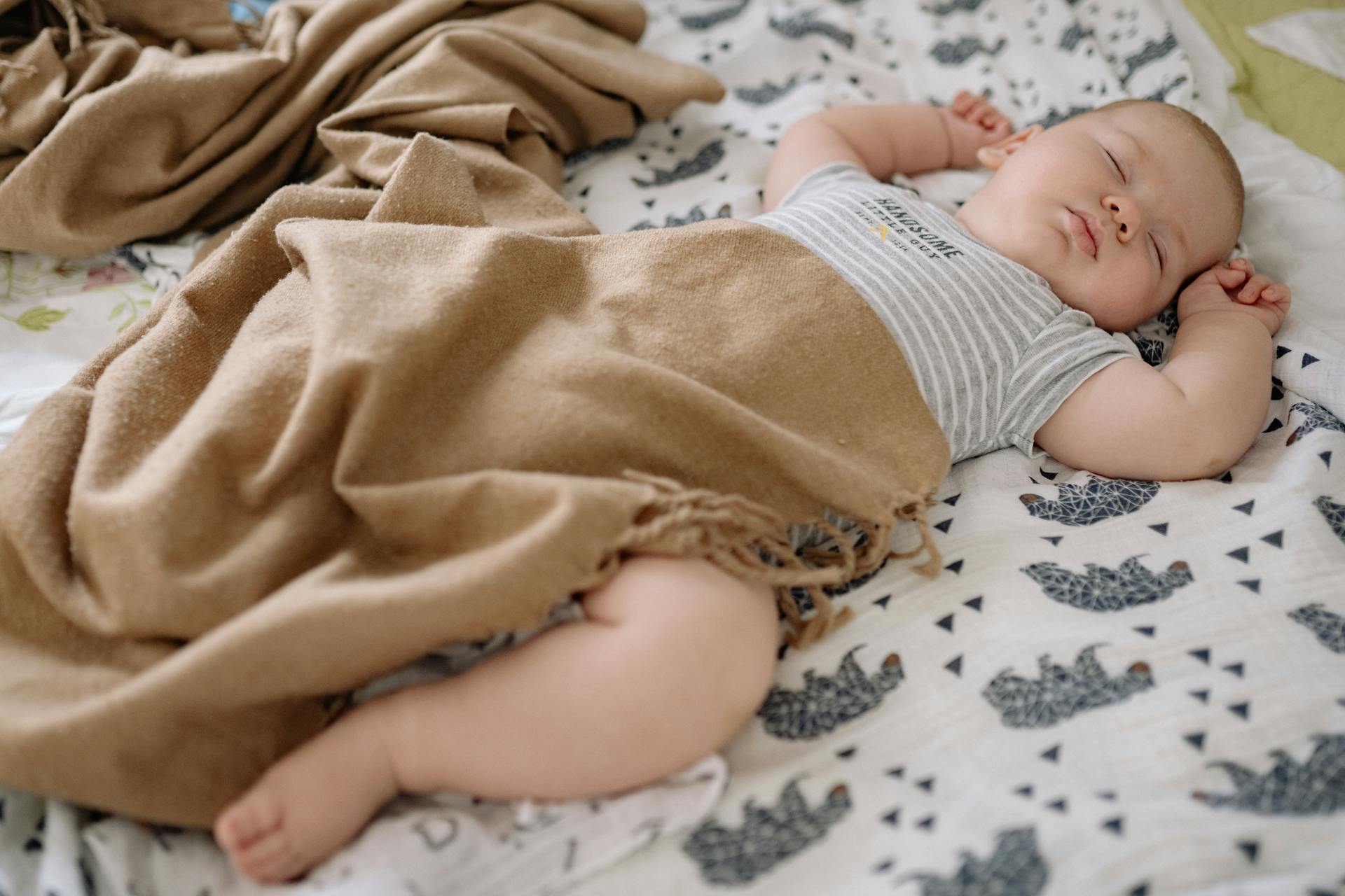 A serene baby sleeping on a patterned blanket, wrapped in a warm brown cover.