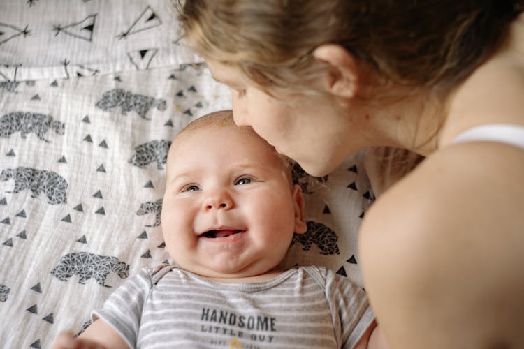 Woman Kissing Baby In White And Gray Stripe Onesie Sleeping