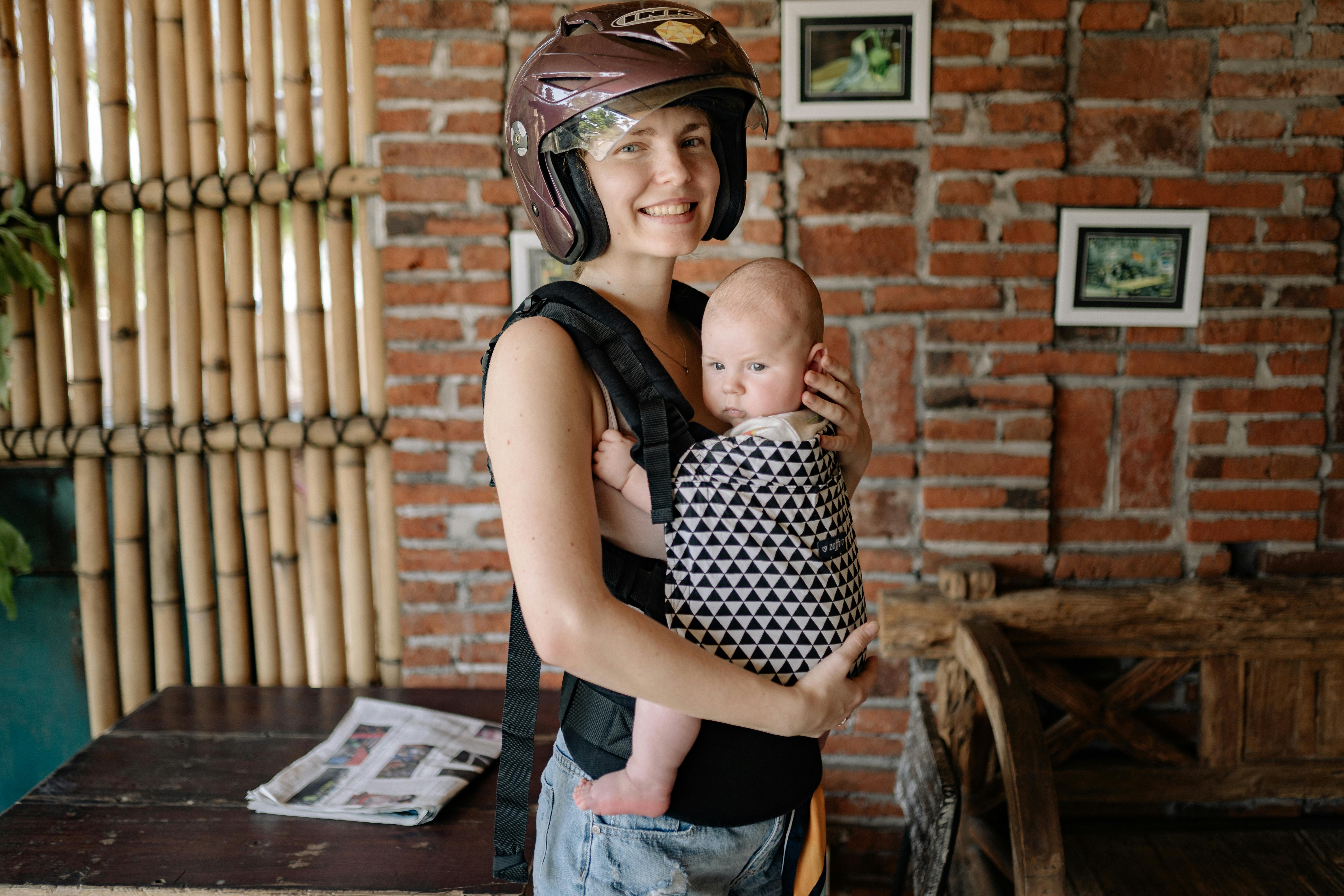 woman wearing brown helmet while carrying her baby