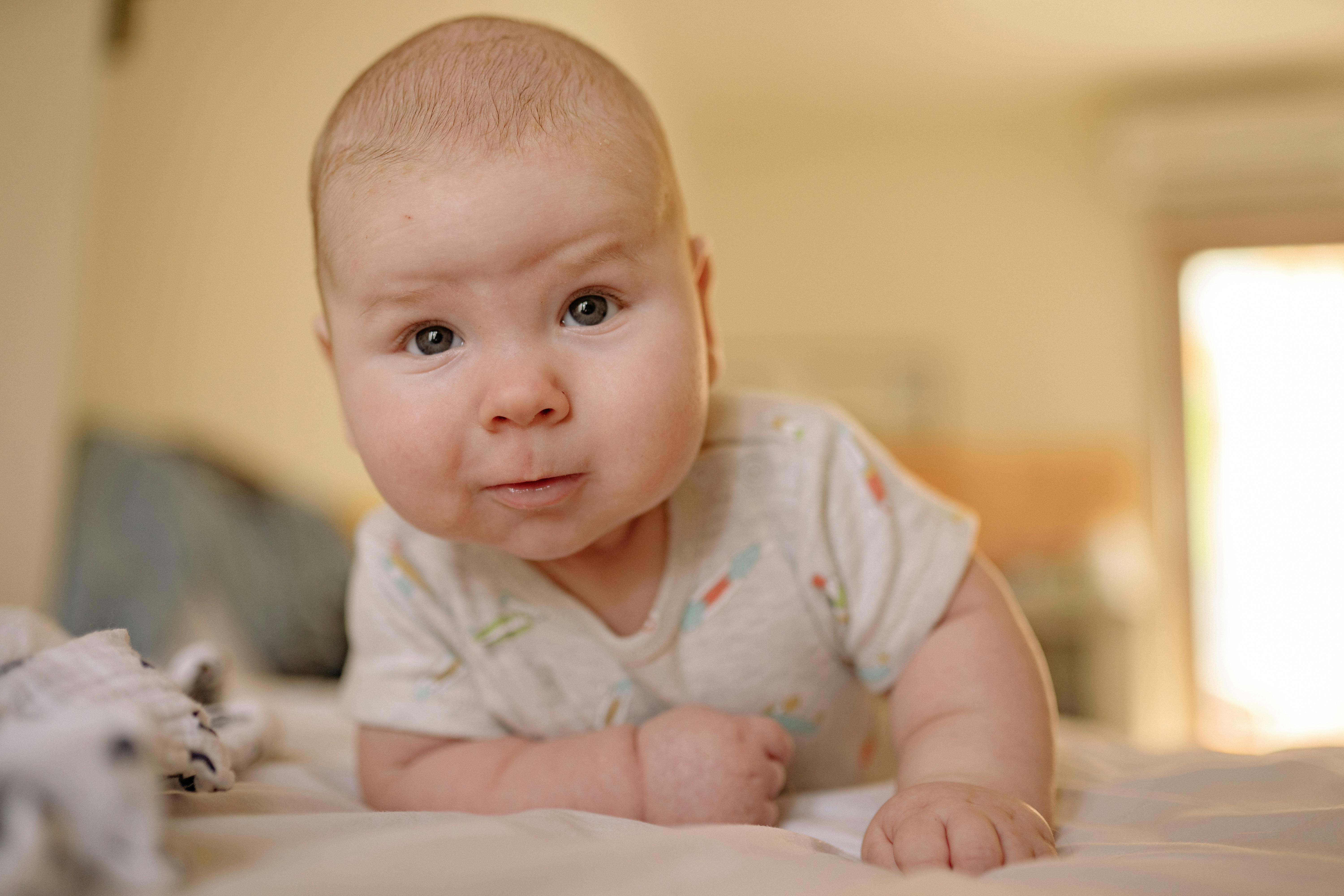 baby in gray onesie lying on bed