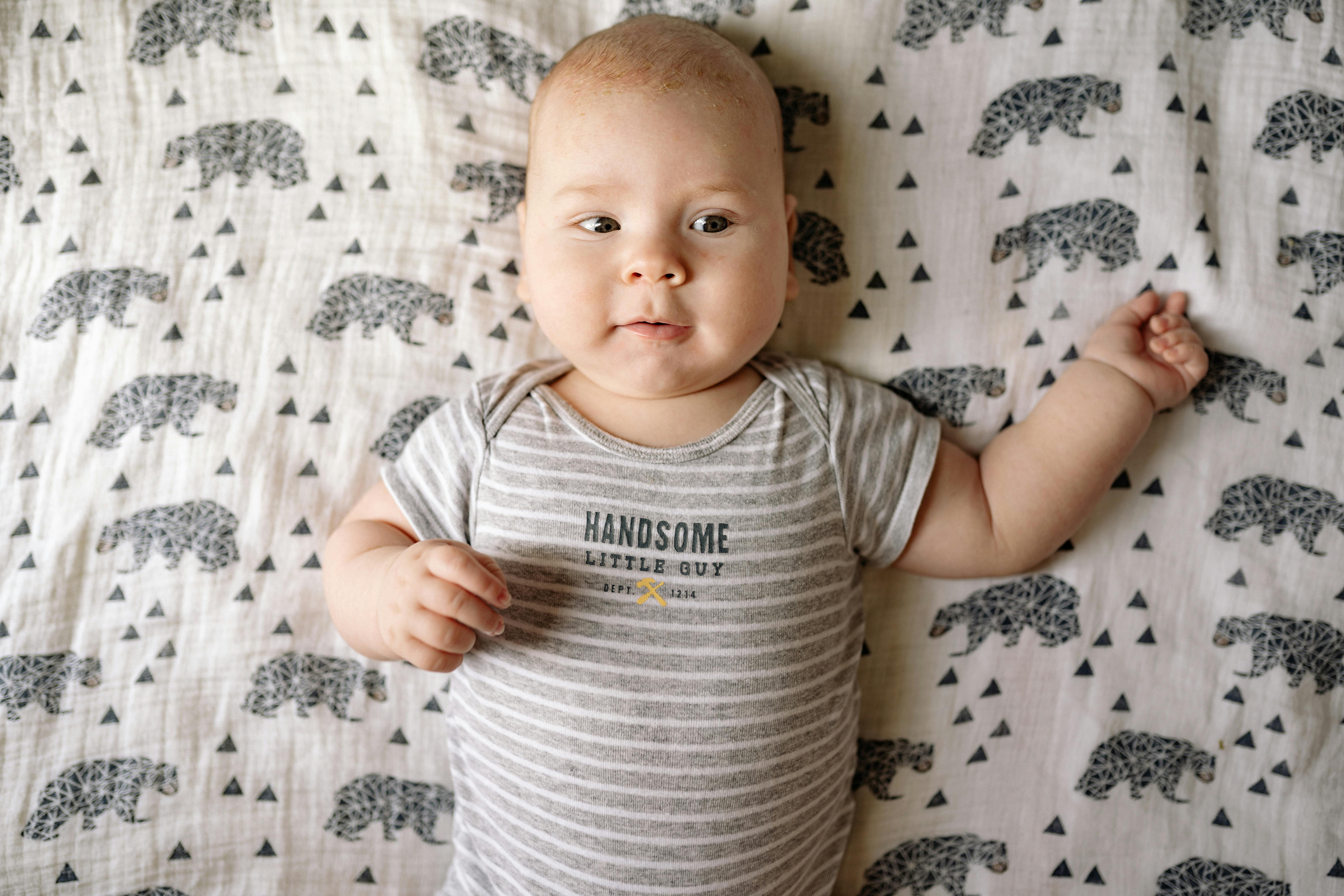 Free Baby in White and Gray Stripe Onesie Lying on White and Black Floral Textile Stock Photo