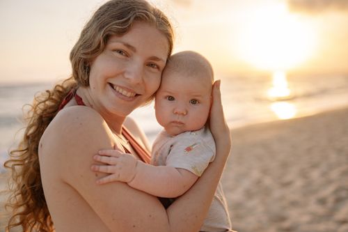 Free A joyful mother holding her baby on the beach during a beautiful sunset. Stock Photo