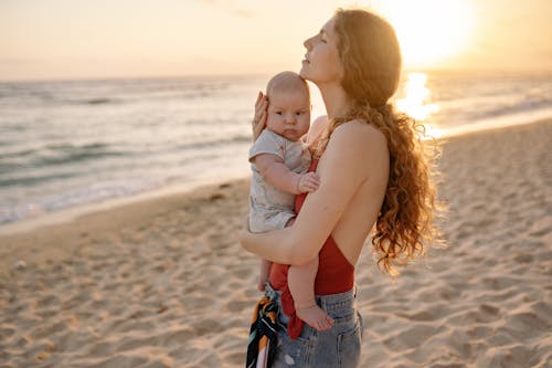 Free Woman Carrying Baby at the Beach during Sunset Stock Photo