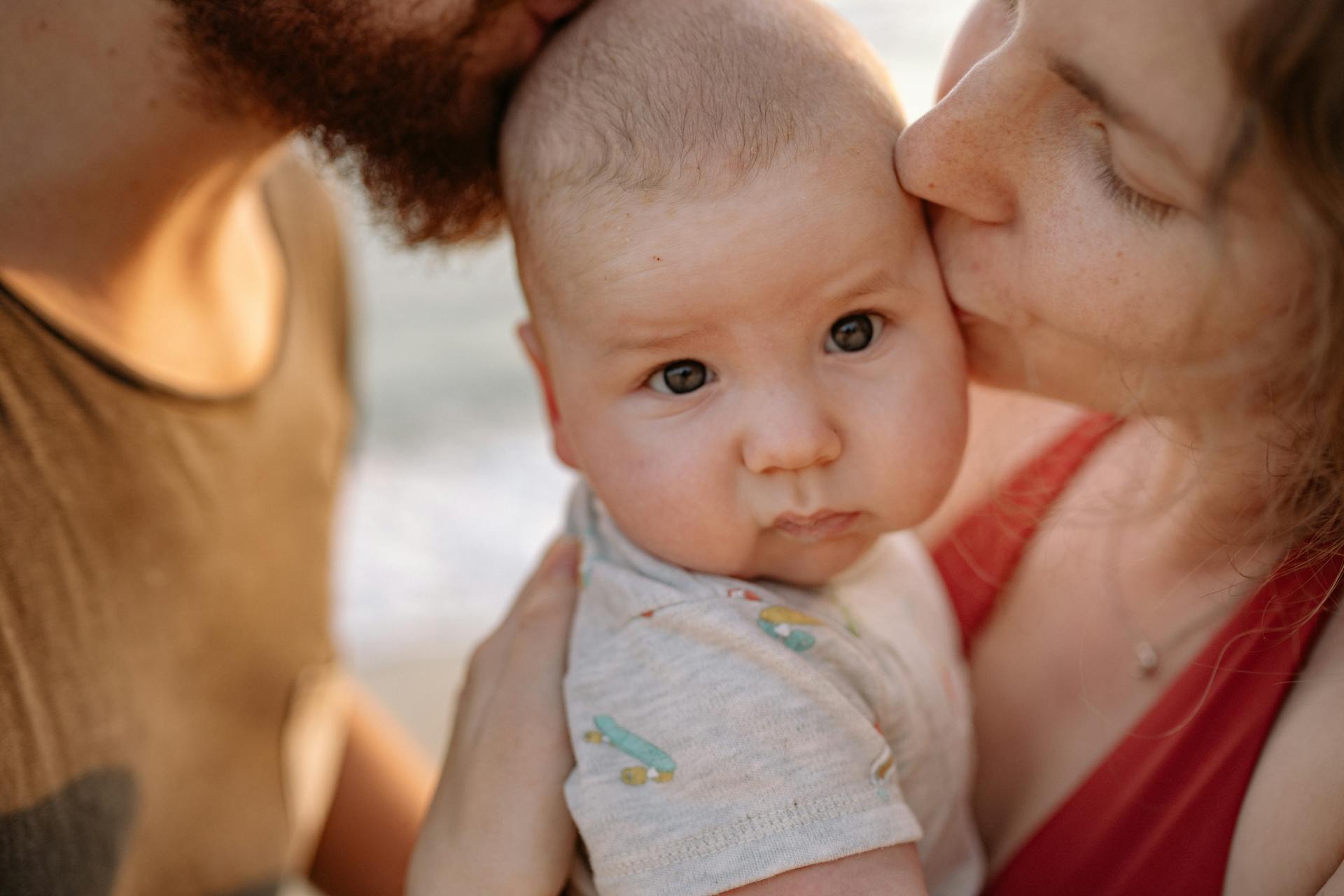 A tender moment of parents kissing their baby, highlighting love and family bonds.