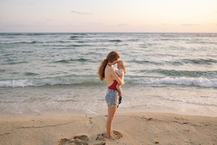 A Mother Carrying Her Baby While Standing On The Beach