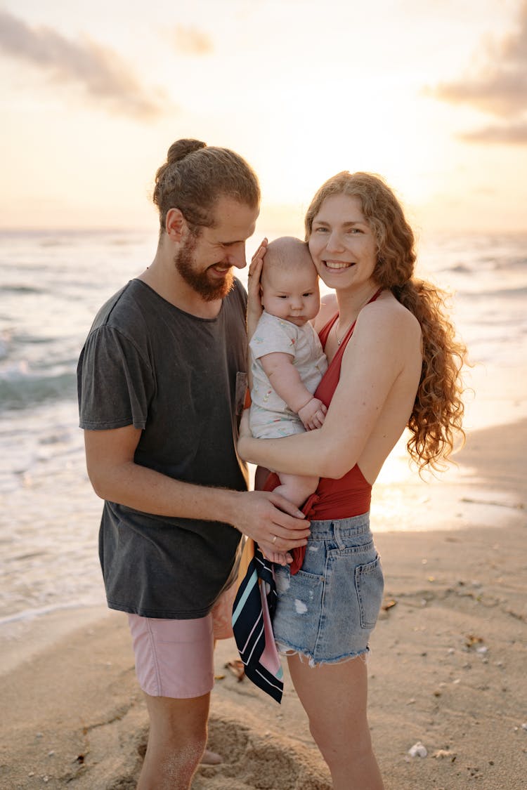 A Family Standing On The Shore During Sunset