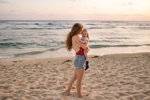 Free Mother holding baby on a beach during sunset, evoking warmth and family bonding. Stock Photo