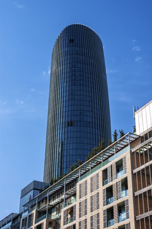 Free Vertical shot of Amman's modern skyline featuring a distinctive cylindrical skyscraper against a clear blue sky. Stock Photo