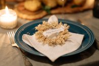 A cozy Thanksgiving table setting featuring a wreath napkin and candlelit ambiance.