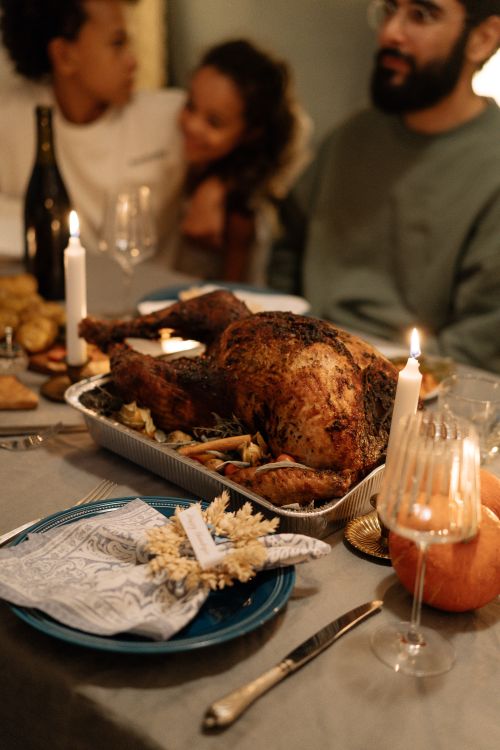 Free Warm Thanksgiving dinner scene with turkey, candles, and family gathered indoors. Stock Photo