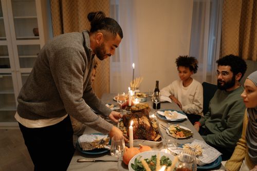Free A family gathered around a dining table enjoying Thanksgiving dinner indoors with candlelit ambiance. Stock Photo