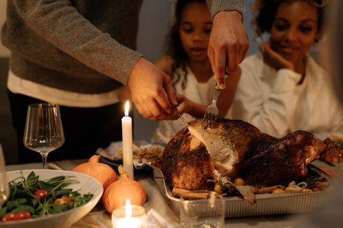 Free Family carving a Thanksgiving turkey at a festive dinner table indoors, warm candlelight. Stock Photo