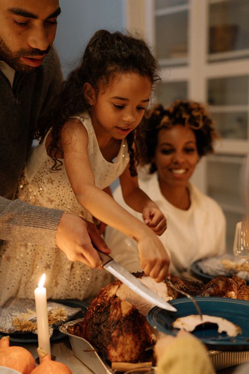 Free A warm family gathering around the table slicing a turkey for Thanksgiving dinner. Stock Photo
